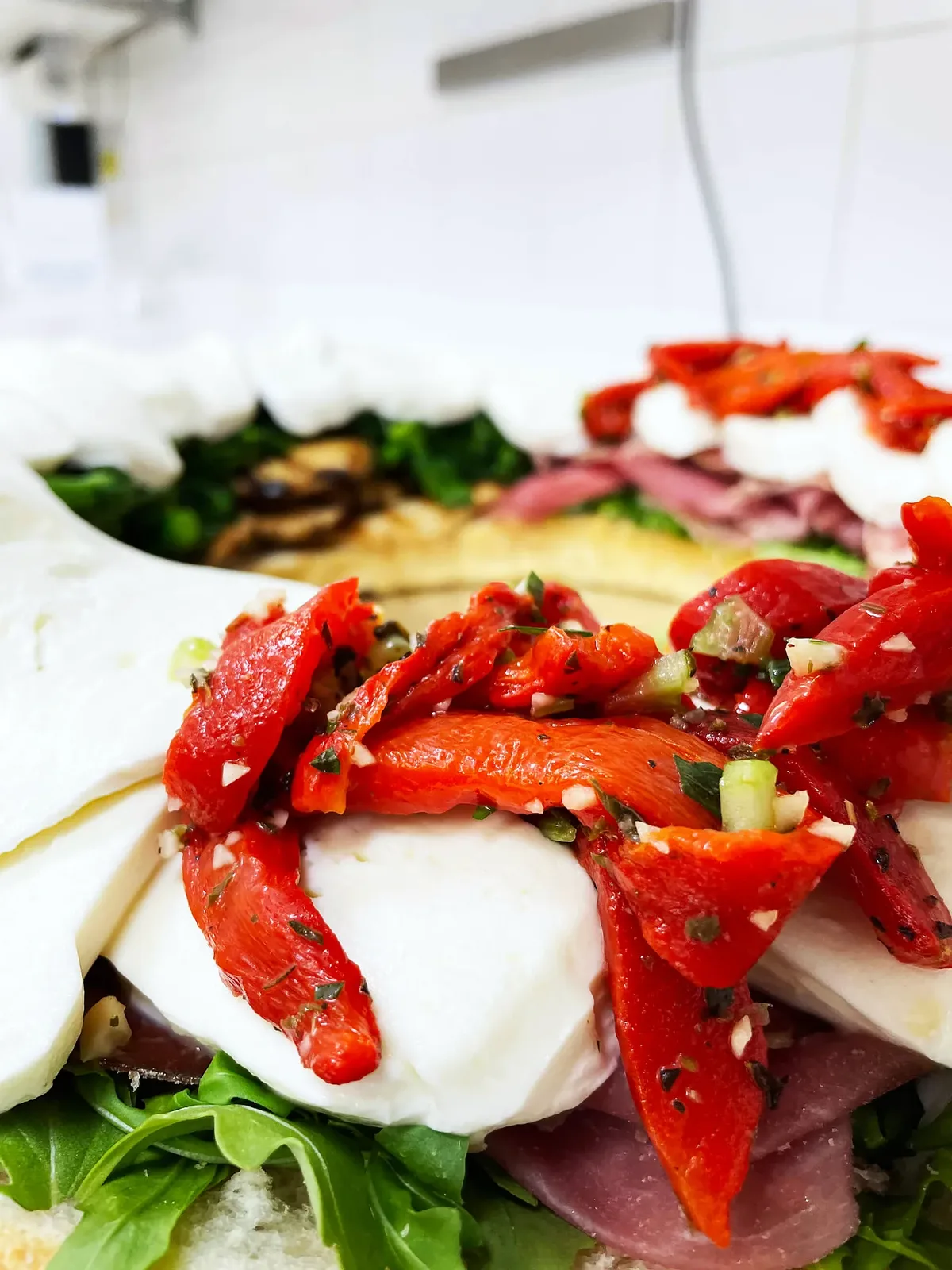 Roasted red peppers over sliced fresh mozzarella with arugula and cured meat