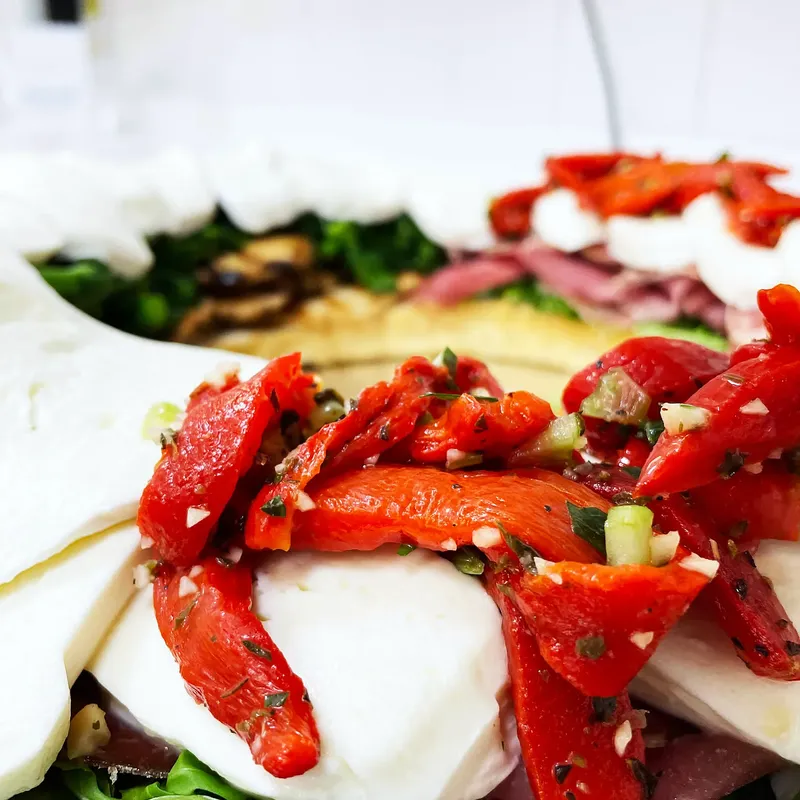 Roasted red peppers over sliced fresh mozzarella with arugula and cured meat